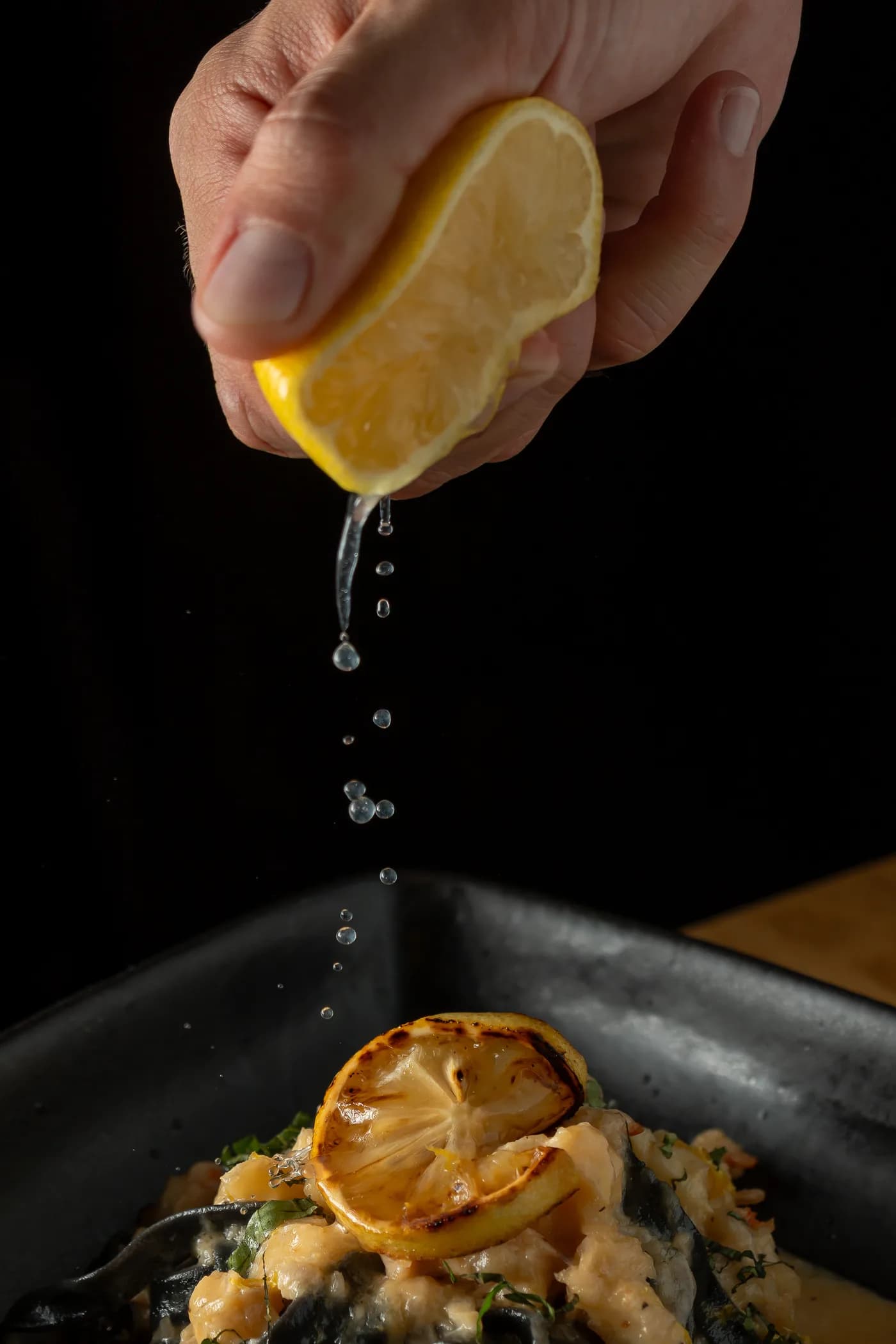 A hand squeezing lemon over a charred-citrus dish