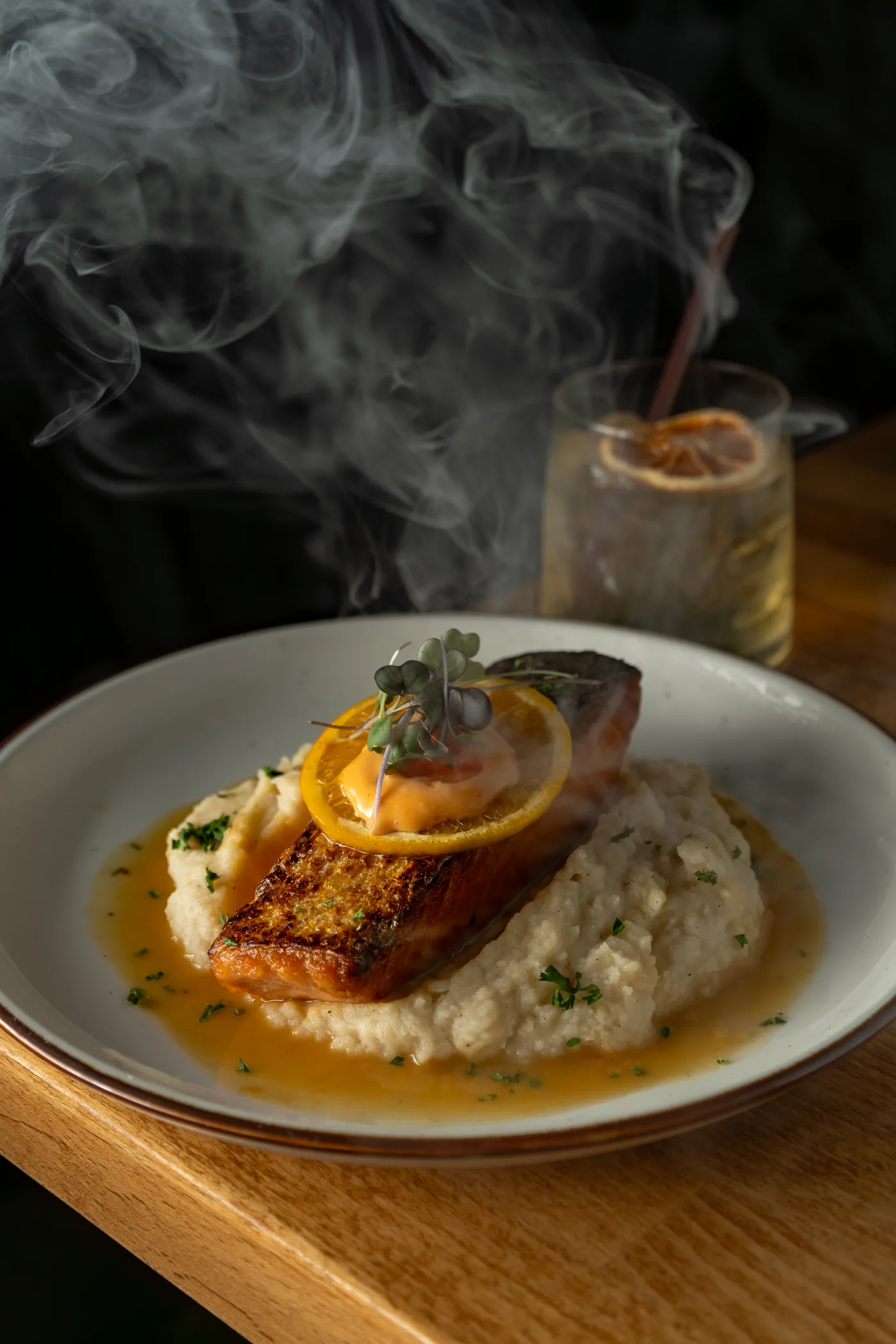 Crispy salmon on purée beside a smoking highball