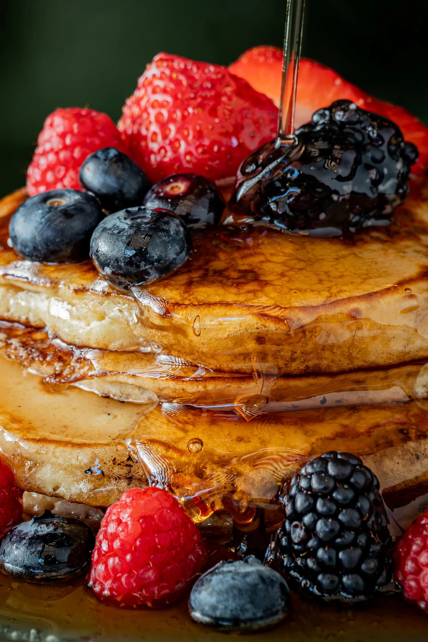 Syrup poured over a stack of berry-topped pancakes