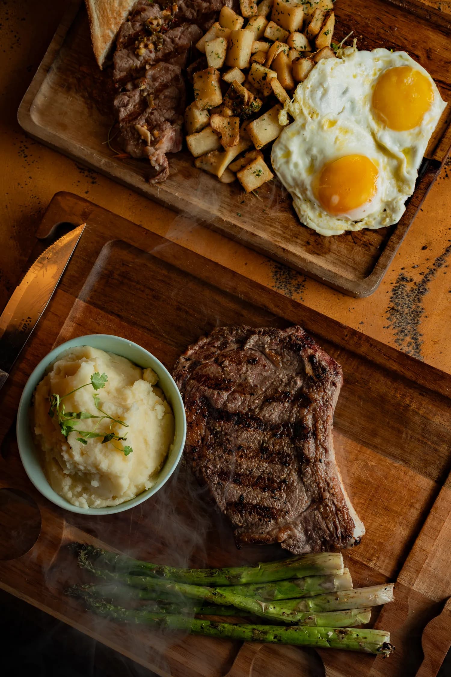 A steak and mashed-potato board with steak and eggs behind