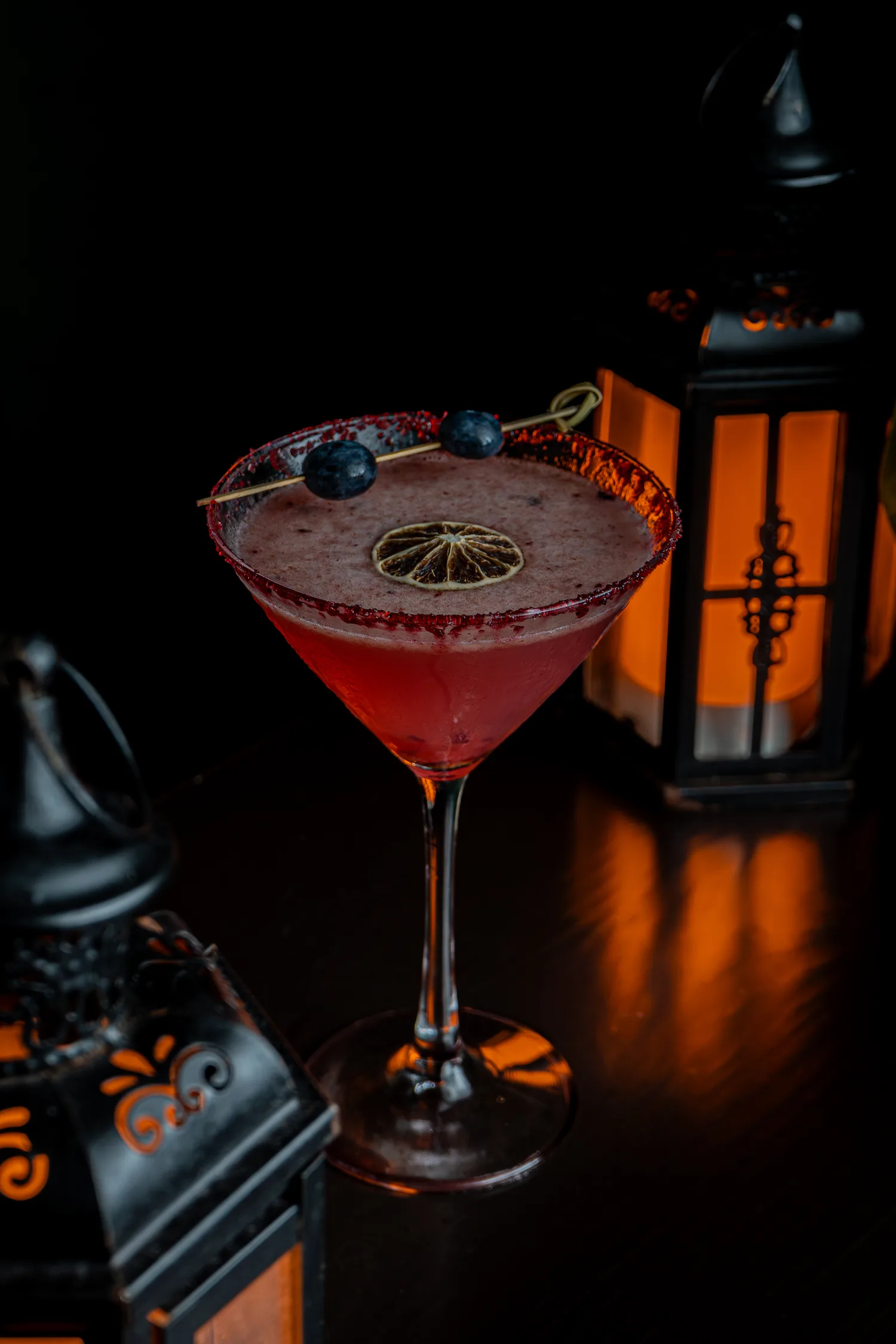 A red cocktail with a citrus-and-blueberry garnish