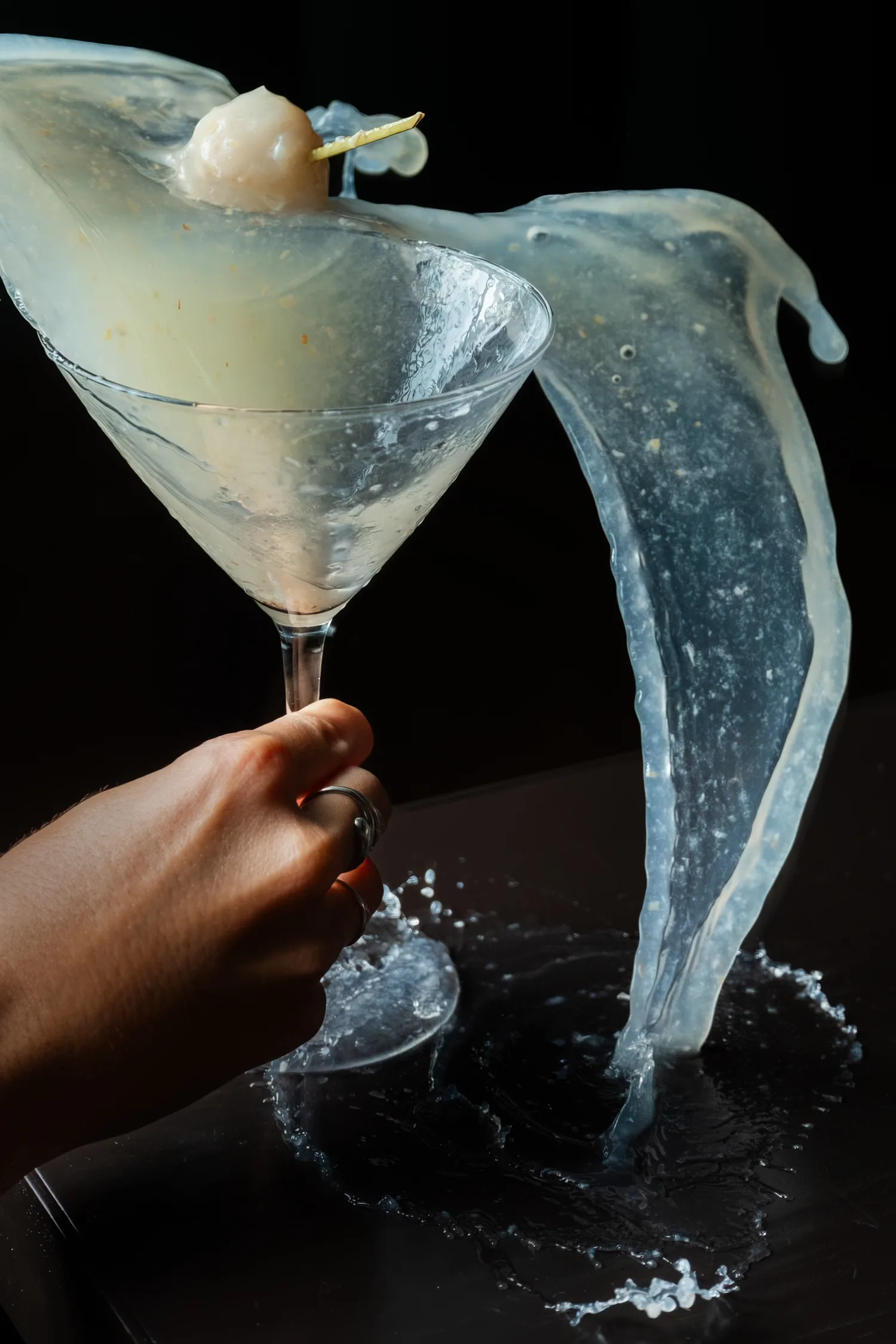 A hand lifting a martini in a dramatic splash of liquid