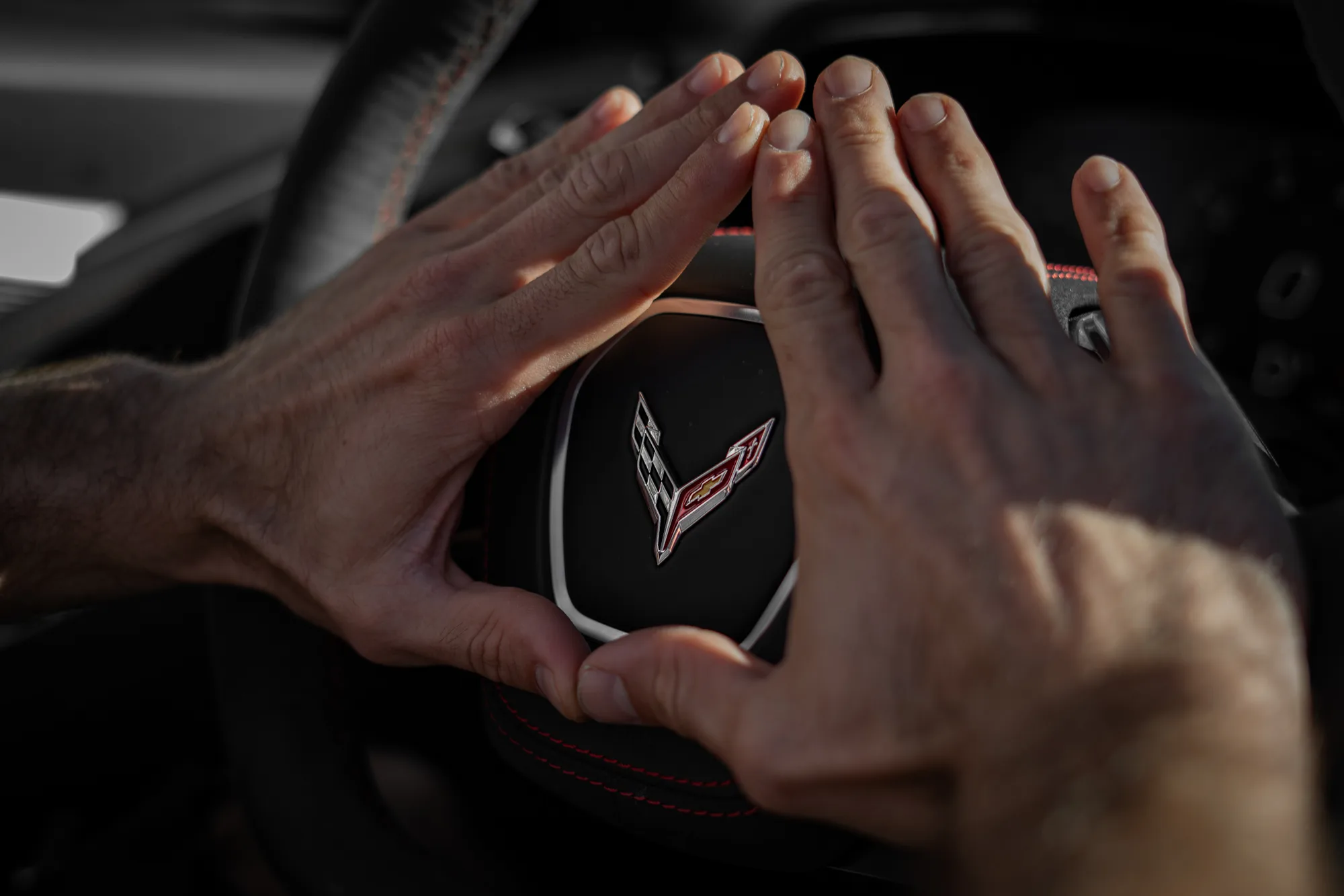 Hands over the Corvette steering wheel and crossed-flags emblem
